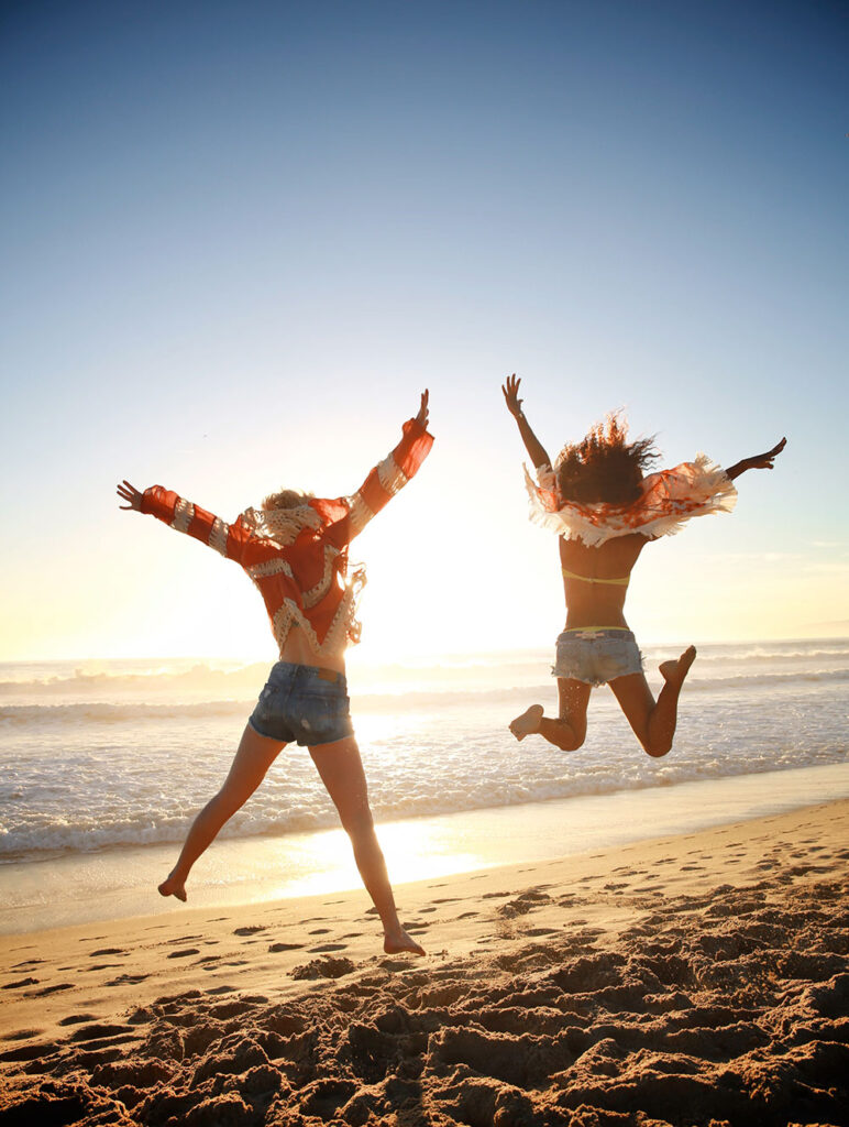Two women jumping on Santa Monica Beach at sunset