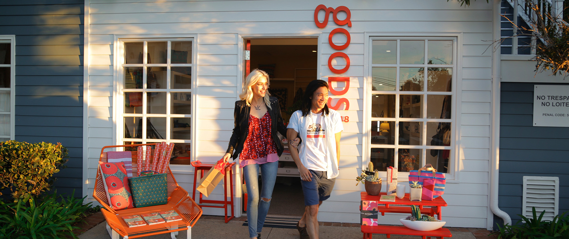 Man and woman holding hands and a bag walking out of a white storefront