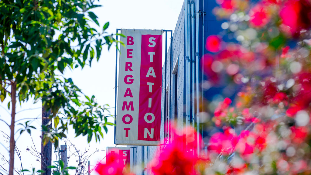Picture of Bergamot Station sign (red and white) with tree and pink flowers in foreground
