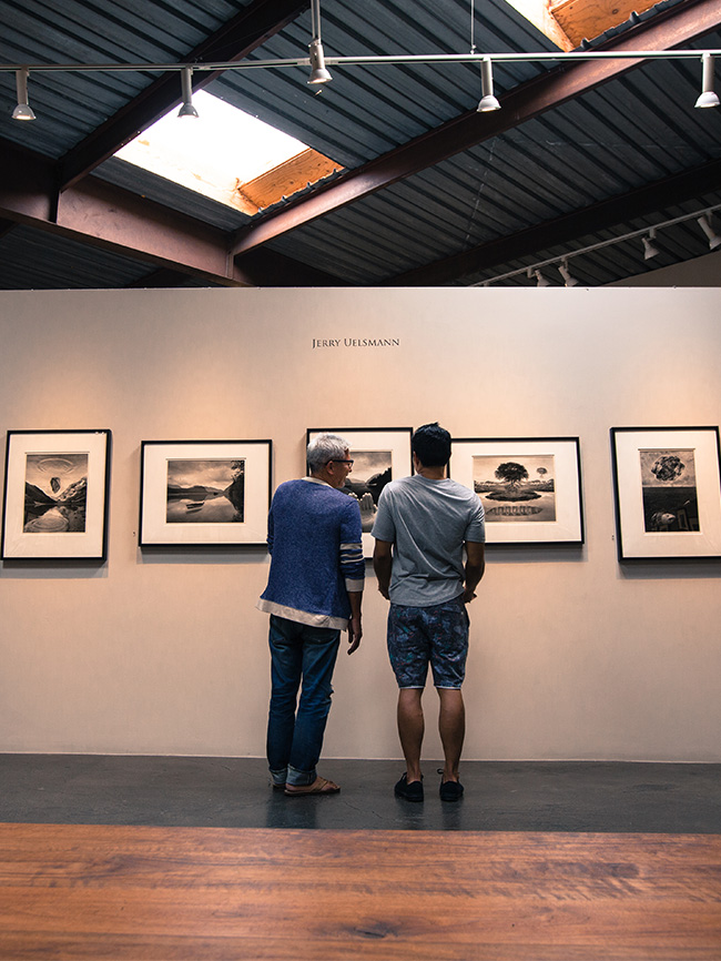 Two men looking at photo in art gallery; pictures hanging in a row on walls