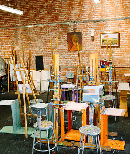 Art Studio with easels, paint brushes and stools; brick wall with hanging art