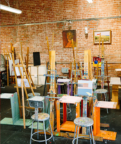 Art Studio with easels, paint brushes and stools; brick wall with hanging art