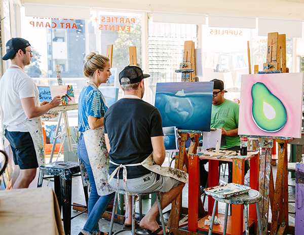 Two people looking at painted art on easel; paint studio with natural lighting