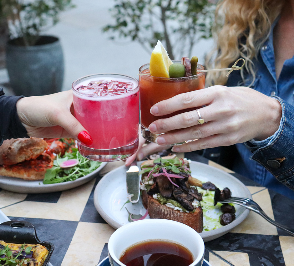 Two people clinking glasses together; plates with brunch food on table