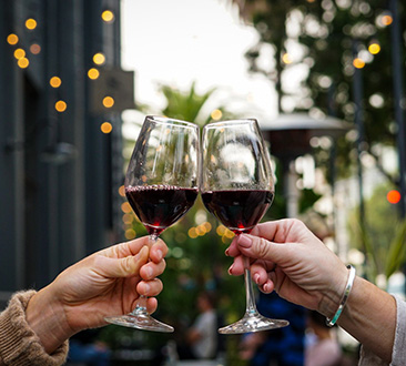 Two female hands clinking glasses of red wine in the air; outdoor