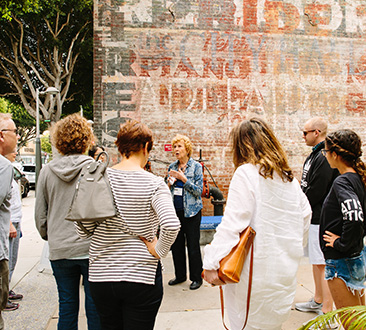 Group listening to woman giving tour; brick wall with dilapidated writing in the background