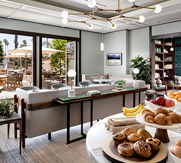 Image of hotel meeting space with natural lighting and indoor/outdoor space; fruit and breakfast spread laid out on bar