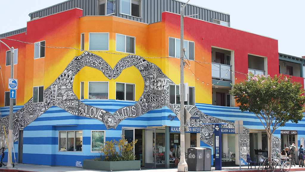 Mural of two hands forming heart; love wins written on hands; red, orange and yellow background