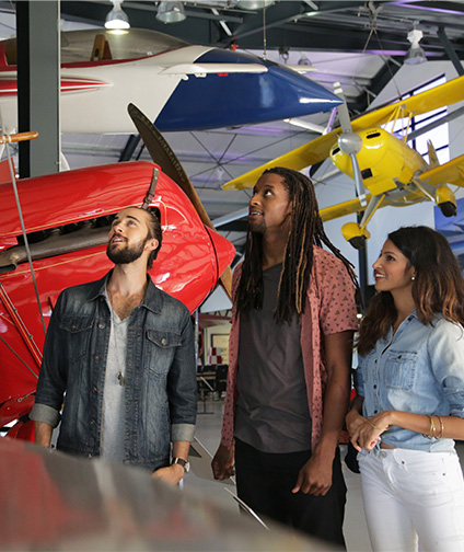 Three people looking up at red airplane in aviation museum