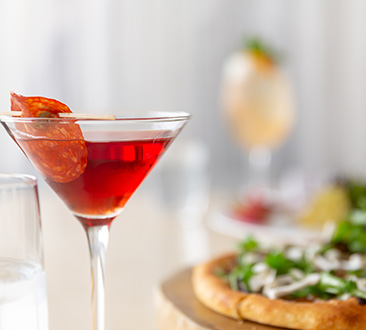 Red martini drink with garnish; pizza in the background