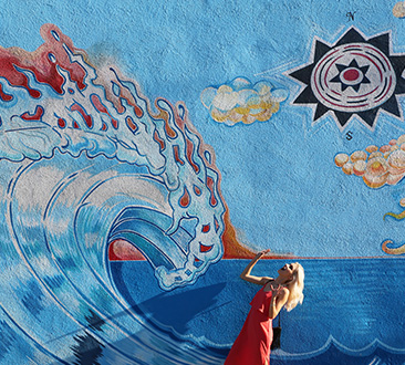 Woman pretending to be scared of wave painted on large wall; street mural