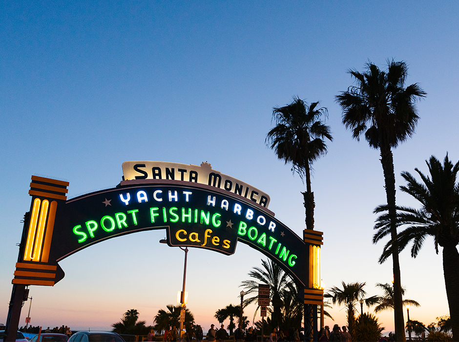 Santa Monica Pier arch at dusk with palm trees.