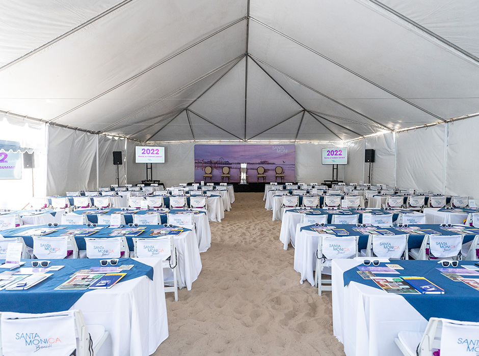 Outdoor tent set up in the sand filled with tables classroom style with elegant white and blue cloth