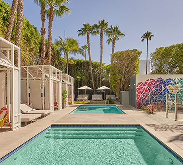 Hotel pool with cabanas on the left and colorful wall on the right; palm trees in background