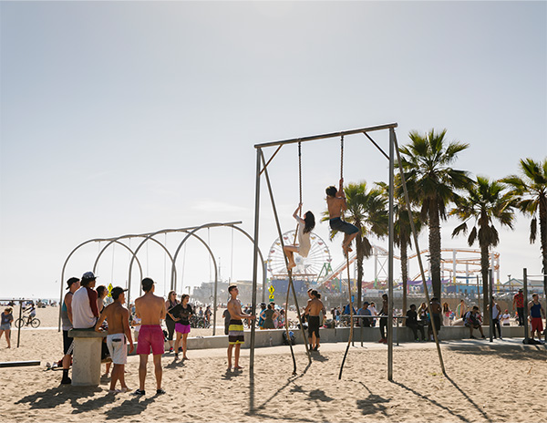 People climbing ropes on beach with Santa Monica Pier in background