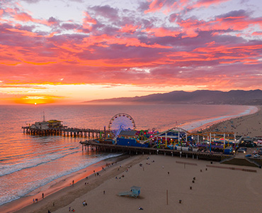 Red, pink, orange and yellow sunset over Santa Monica Pier; Santa Monica Beach aerial shot over Santa Monica Pier