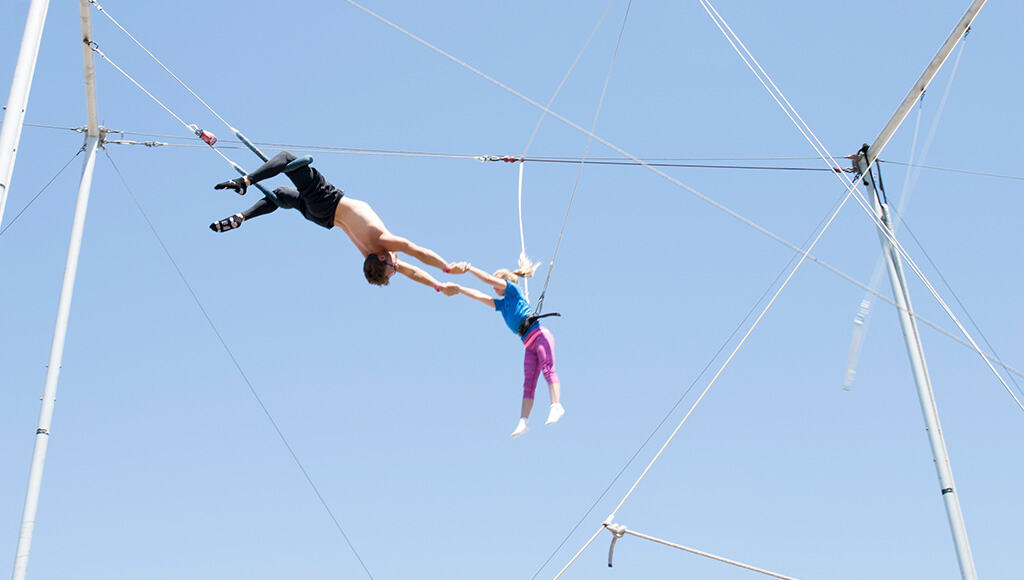 Picture of man hanging upside down from trapeze swing holding little girl's arms
