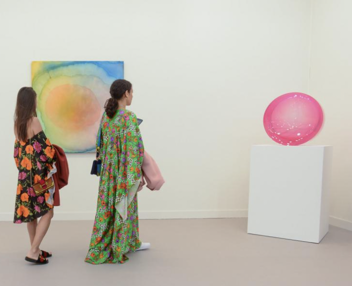 Two woman admiring pink circular artwork in corner of gallery