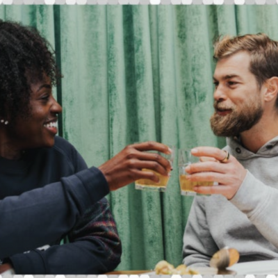 Picture of man and woman clinking glasses with teal curtain in background